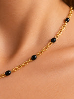 kettenglieder-detail.jpgNahaufnahme der Nivra mit glänzenden schwarzen Perlen und ineinandergreifenden goldfarbenen Kettengliedern auf der Haut.