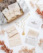 MERCY'S Ritual-Paket Flatlay: Geöffnete Premium-Box mit Samtpouch, goldener Halskette, Manifest-Karte, Poliertuch und Schmuckpflegekarte, dekoriert mit Trockenblumen