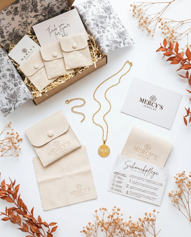 MERCY'S Ritual-Paket Flatlay: Geöffnete Premium-Box mit Samtpouch, goldener Halskette, Manifest-Karte, Poliertuch und Schmuckpflegekarte, dekoriert mit Trockenblumen
