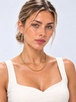 Porträt eines Models mit goldfarbener Kordelkette Tharien und weißem Trägertop vor hellem Hintergrund.