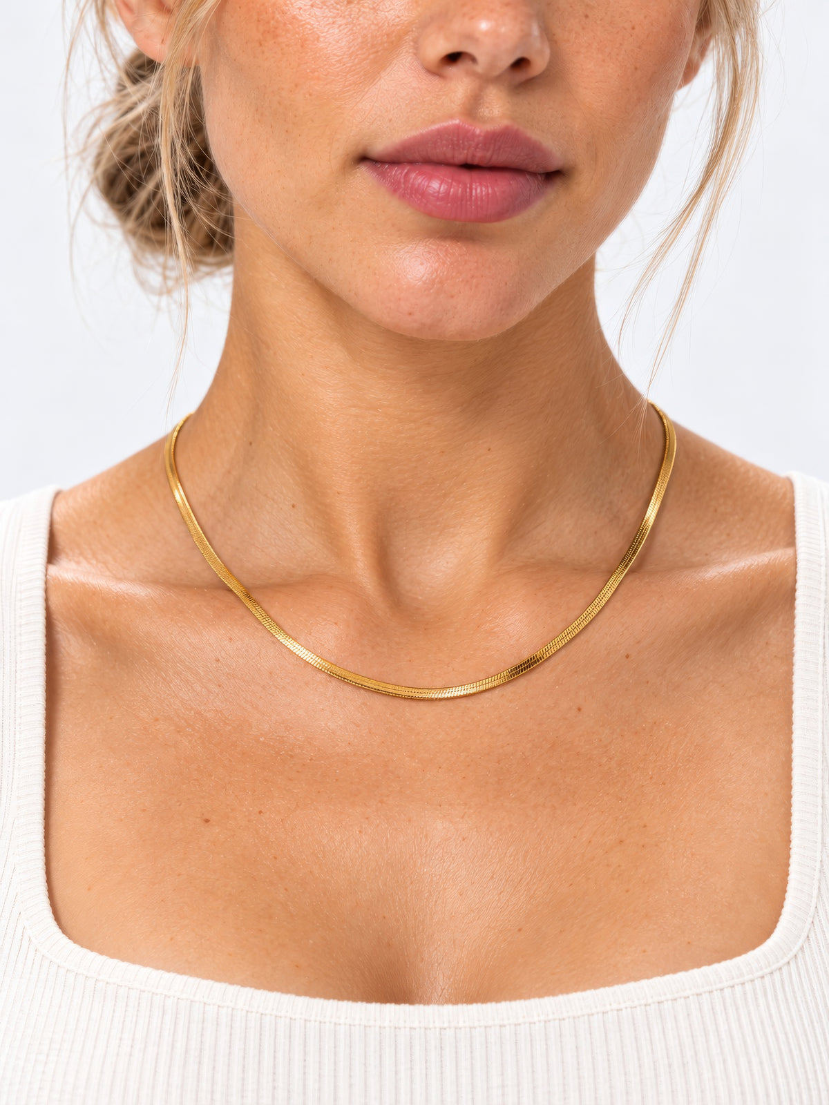 Goldene Velira-Schlangenkette am Hals eines Models, getragen zu einem weißen Top in Nahaufnahme.