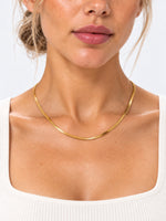 Goldene Velira-Schlangenkette am Hals eines Models, getragen zu einem weißen Top in Nahaufnahme.
