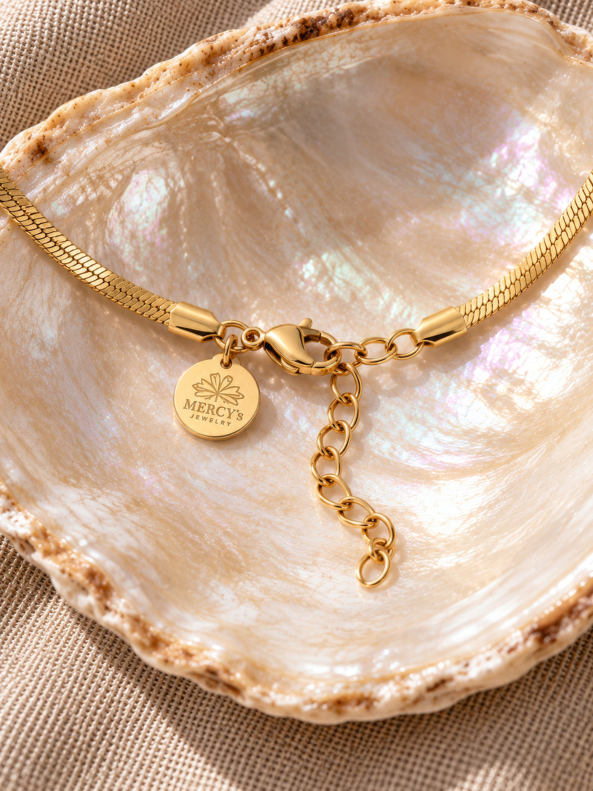 Karabinerverschluss der Velira-Schlangenkette mit Verlängerungskette und graviertem Mercy’s-Jewelry-Plättchen auf einer Muschel.