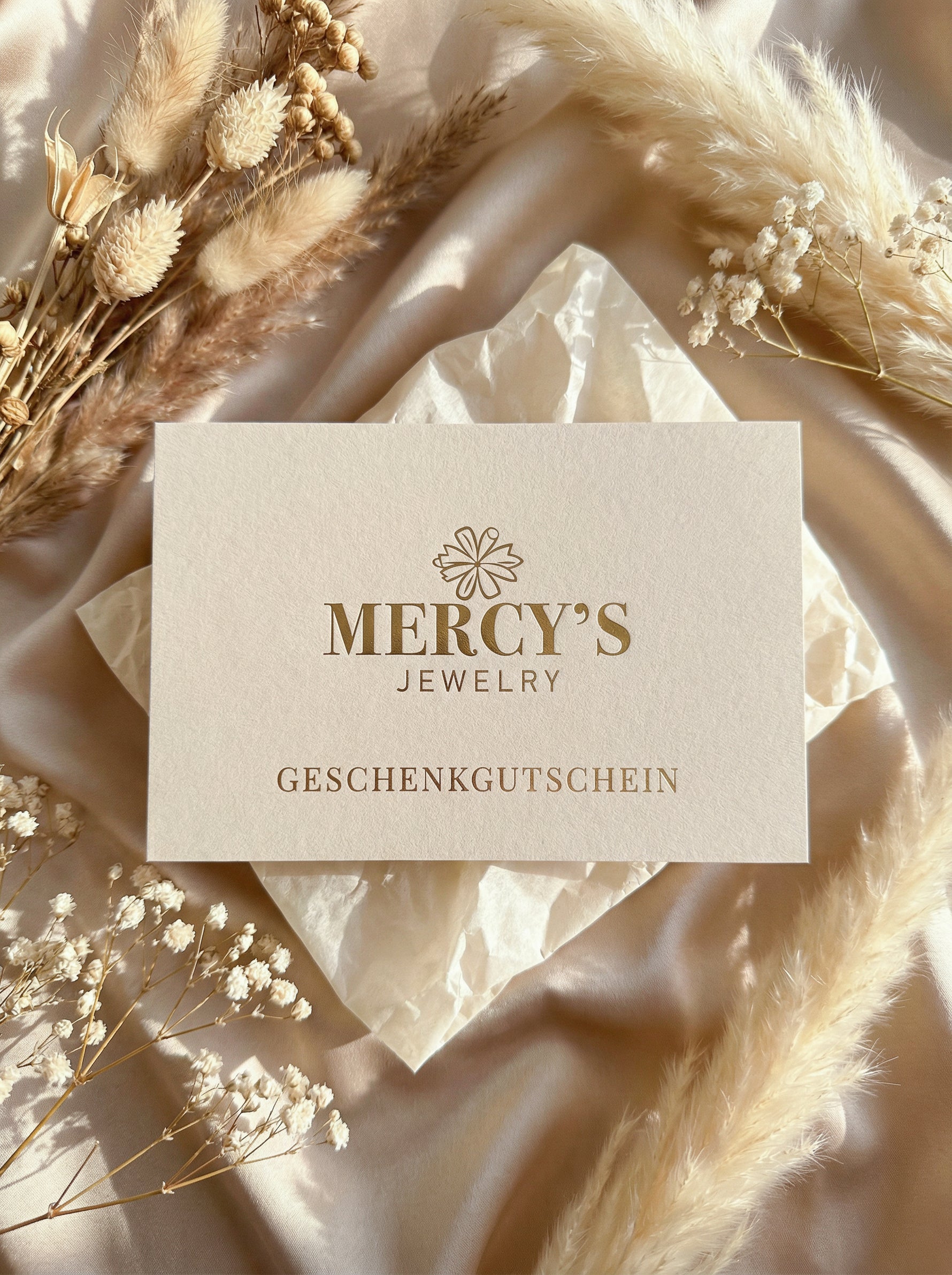 Mercy’s Jewelry Geschenkgutschein als Produktfoto, auf satiniertem Stoff mit Pampasgras und Schleierkraut dekoriert
