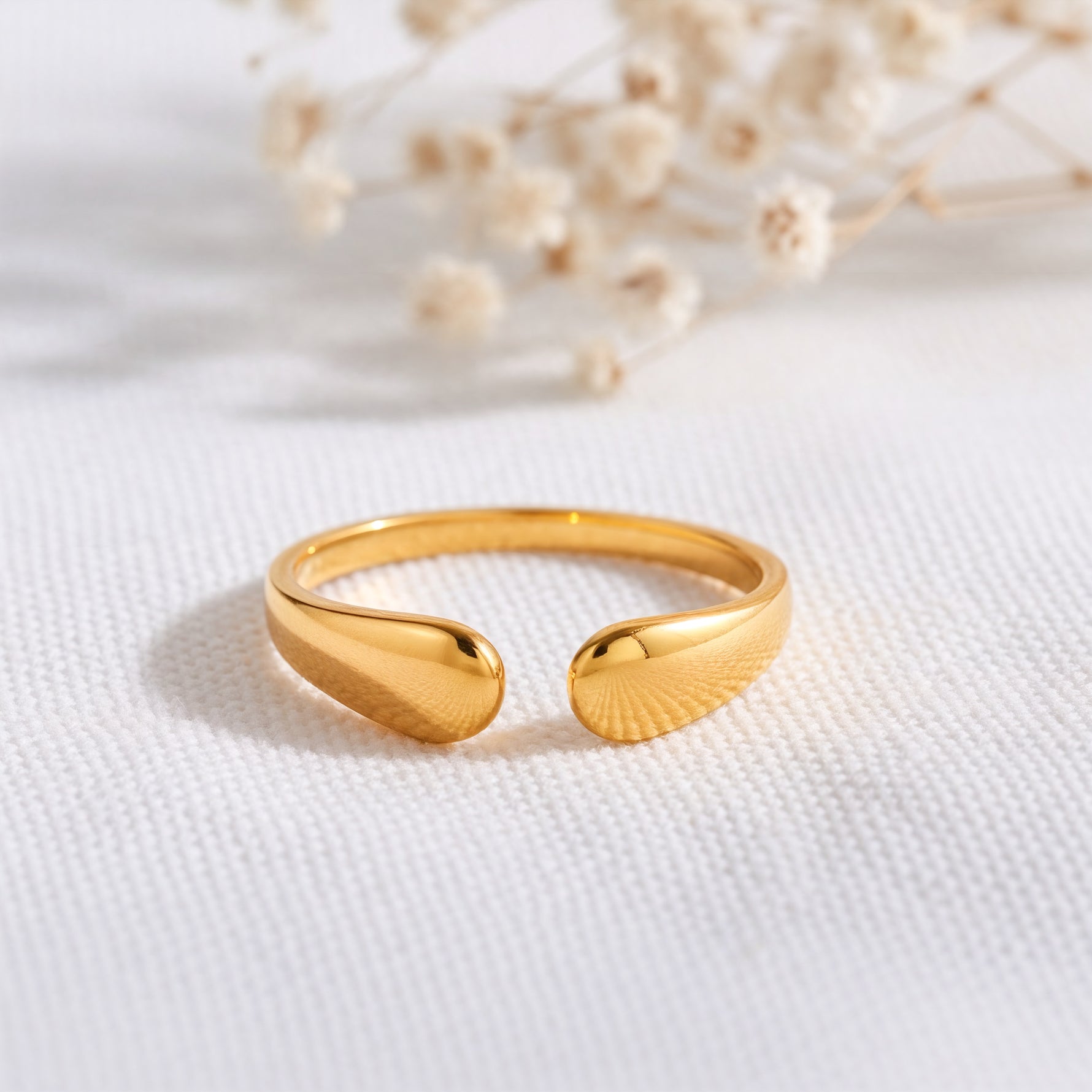 Offener Ring aus Edelstahl 18 K vergoldet, mit eleganter Tropfenform auf hellem Stoff mit Trockenblumen im Hintergrund – Amelina Ring | Mercy’s Jewelry