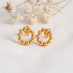 Kreisförmige Ohrstecker mit Kugel-Design aus Edelstahl 18 K vergoldet, liegen auf hellem Stoff mit Trockenblumen im Hintergrund – Orira Studs | Mercy’s Jewelry