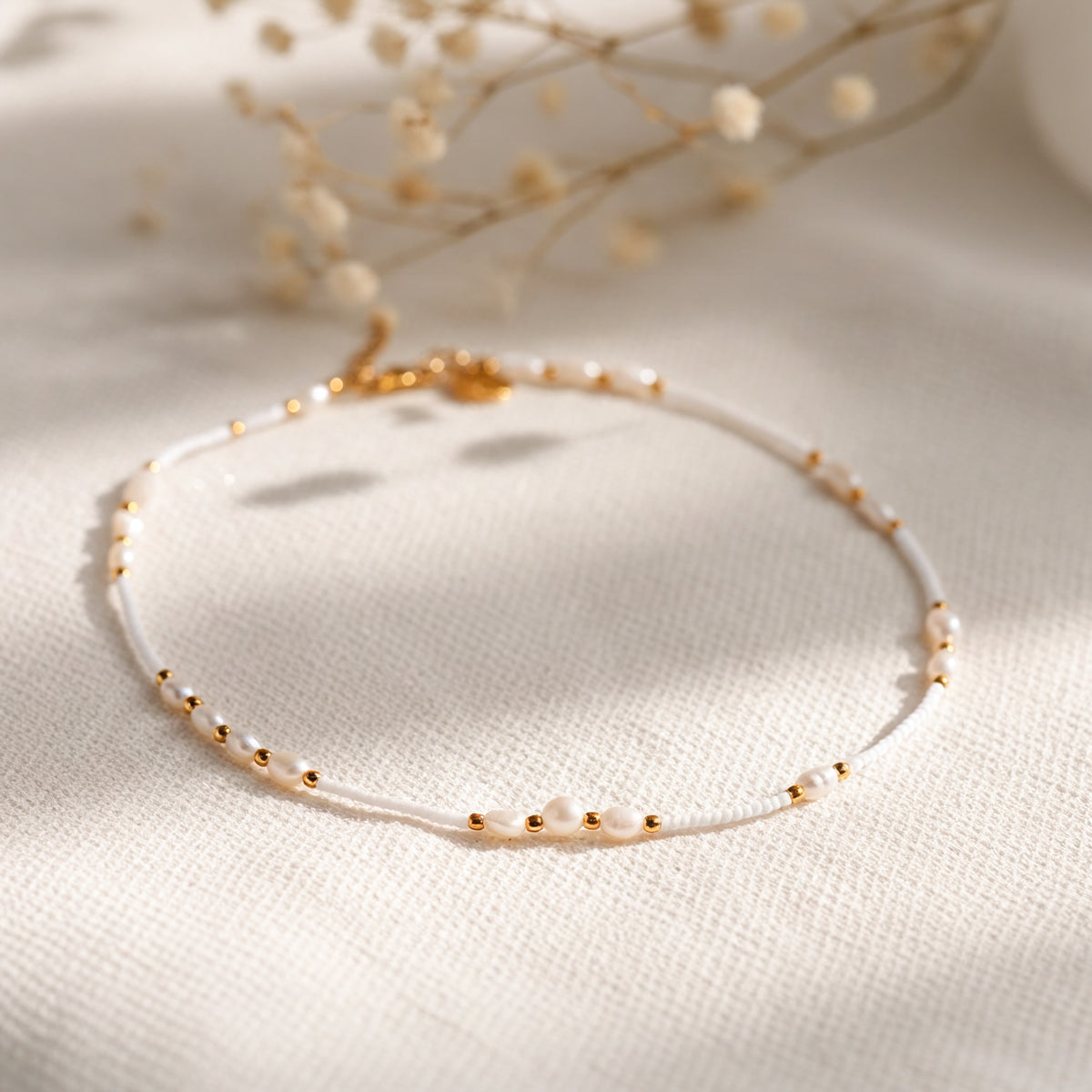 Feine Perlen-Halskette mit goldenen Elementen aus Edelstahl 18 K vergoldet, liegt auf weißem Stoff mit getrockneten Blumen – Mirelin Halskette | Mercy’s Jewelry