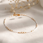 Feine Perlen-Halskette mit goldenen Elementen aus Edelstahl 18 K vergoldet, liegt auf weißem Stoff mit getrockneten Blumen – Mirelin Halskette | Mercy’s Jewelry