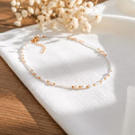 Feine Perlen-Halskette mit goldenen Elementen aus Edelstahl 18 K vergoldet, liegt auf weißem Stoff mit Holzhintergrund und getrockneten Blumen – Mirelin Halskette | Mercy’s Jewelry