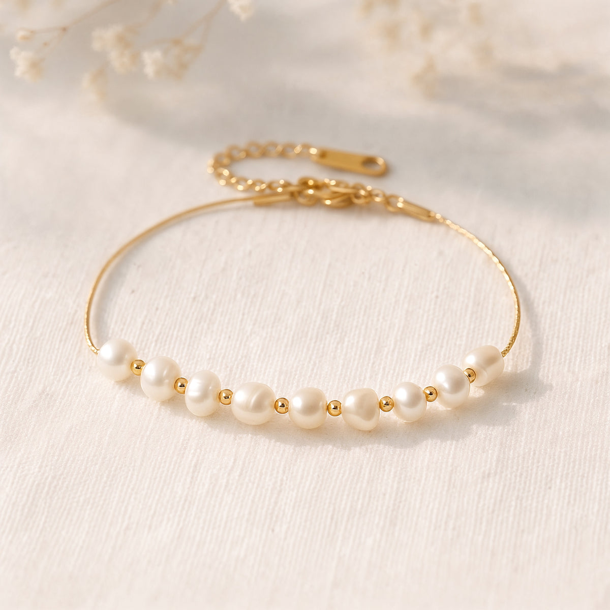 Perlenarmband aus Edelstahl 18 K vergoldet mit feinen Süßwasserperlen und goldenen Zwischenelementen, liegend auf hellem Stoff im warmen Tageslicht – Noelia Armband | Mercy’s Jewelry