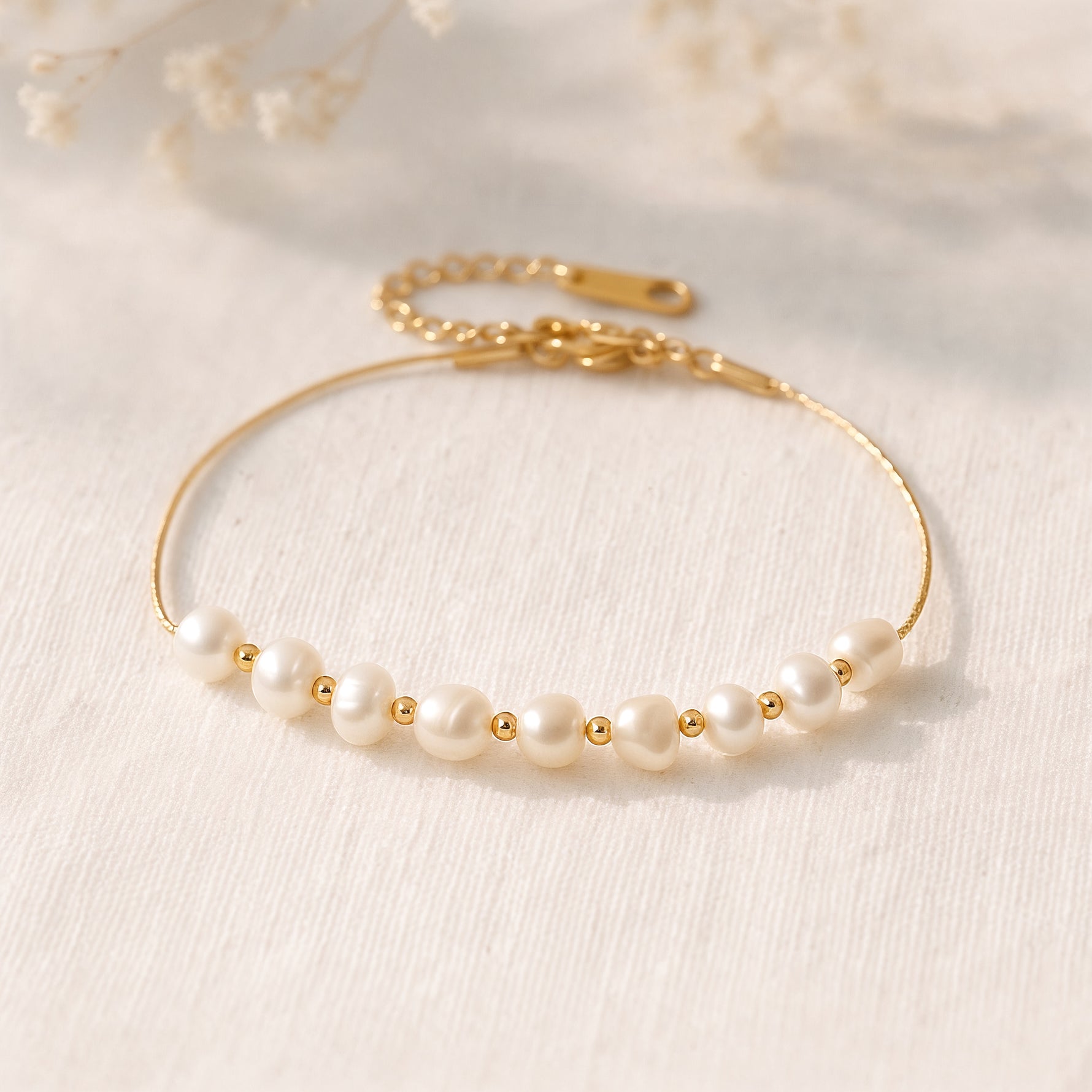 Perlenarmband aus Edelstahl 18 K vergoldet mit feinen Süßwasserperlen und goldenen Zwischenelementen, liegend auf hellem Stoff im warmen Tageslicht – Noelia Armband | Mercy’s Jewelry