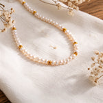 Perlenhalskette mit goldenen Zwischenelementen aus Edelstahl 18 K vergoldet, liegt auf weißem Stoff mit Trockenblumen im Hintergrund – Orielle Perlenkette | Mercy’s Jewelry