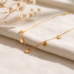 Feine Plättchen-Halskette aus Edelstahl 18 K vergoldet, liegt auf hellem Stoff mit Trockenblumen im Hintergrund – Kaira Halskette | Mercy’s Jewelry