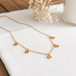 Plättchen-Halskette aus Edelstahl 18 K vergoldet, liegt auf weißem Stoff mit Trockenblumen und Vase im Hintergrund – Kaira Halskette | Mercy’s Jewelry