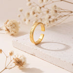 Ring aus Edelstahl 14 K vergoldet, offen und verstellbar, stehend auf heller Steinplatte mit Trockenblumen im Hintergrund – Luneth Ring | Mercy’s Jewelry