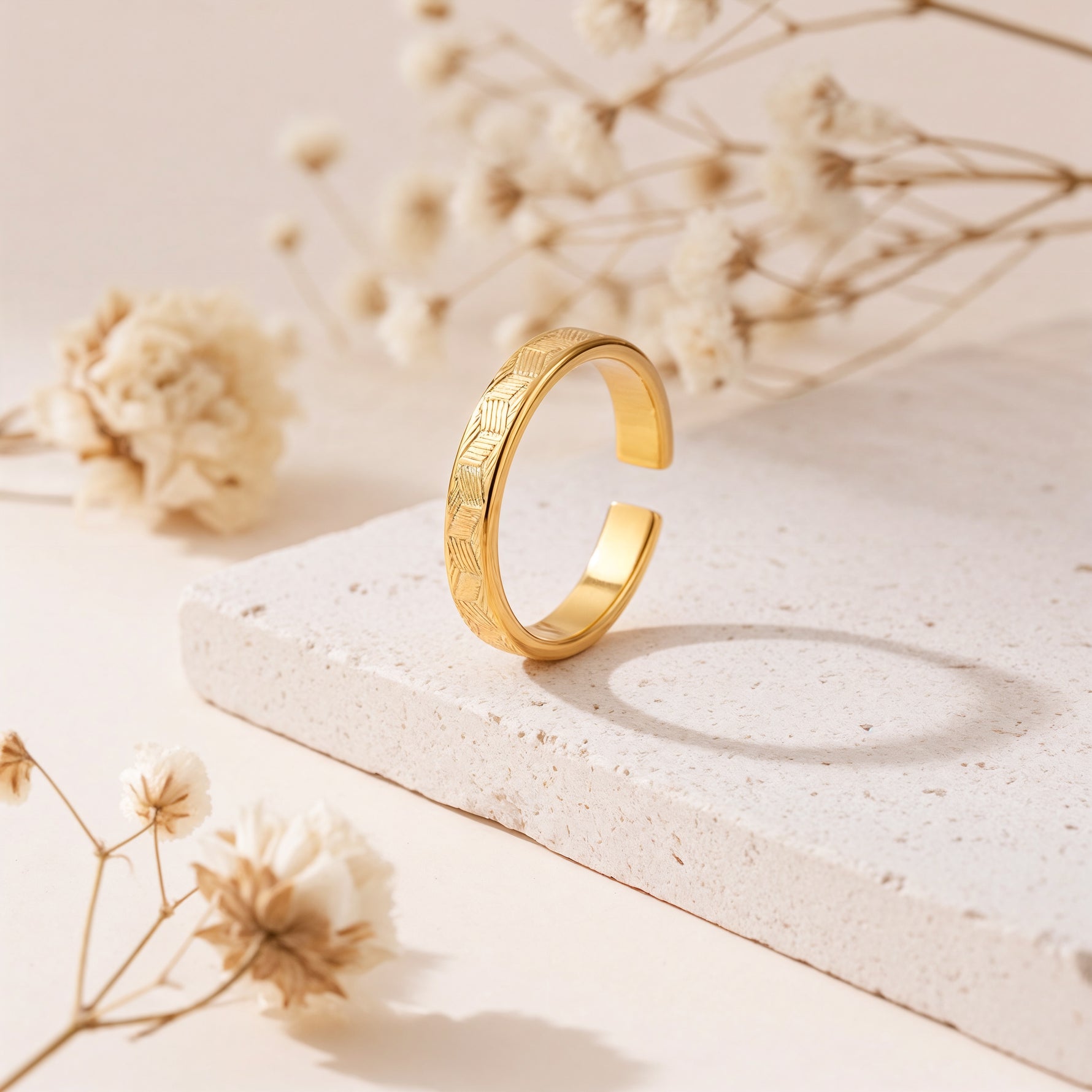 Ring aus Edelstahl 14 K vergoldet, offen und verstellbar, stehend auf heller Steinplatte mit Trockenblumen im Hintergrund – Luneth Ring | Mercy’s Jewelry