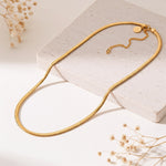 Schlangen-Halskette aus Edelstahl 18 K vergoldet, liegt auf heller Steinplatte mit Trockenblumen – Soleya Halskette | Mercy’s Jewelry