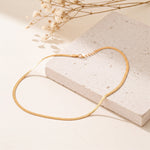 Schlangenkette aus Edelstahl 18 K vergoldet, liegt auf heller Steinplatte mit getrockneten Blumen im Hintergrund – Velira Halskette | Mercy’s Jewelry