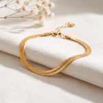 Flaches Schlangenketten-Armband aus Edelstahl 18 K vergoldet, elegant auf hellem Stoff mit Trockenblumen im Hintergrund – Velira Armband | Mercy’s Jewelry