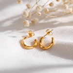 Schlichte Creolen aus Edelstahl 18 K vergoldet mit glänzendem Finish, liegen auf hellem Stoff mit Trockenblumen im Hintergrund – Maeris Creolen | Mercy’s Jewelry