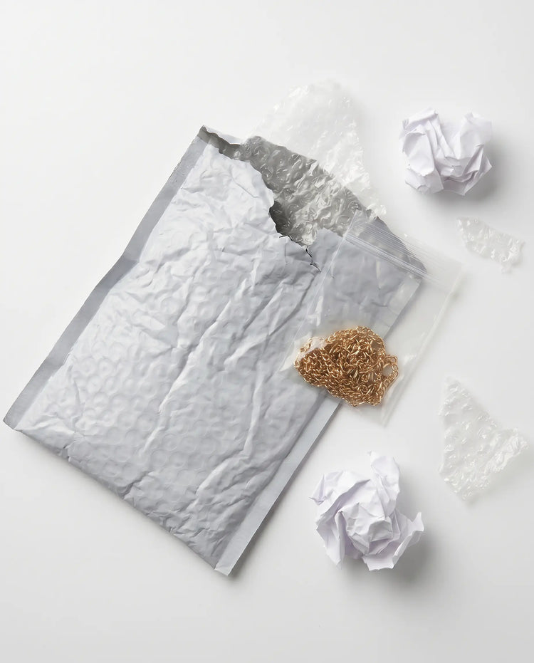 Typische Schmucklieferung anderer Shops: Grauer Polsterumschlag mit Plastiktütchen und goldener Kette ohne Branding
