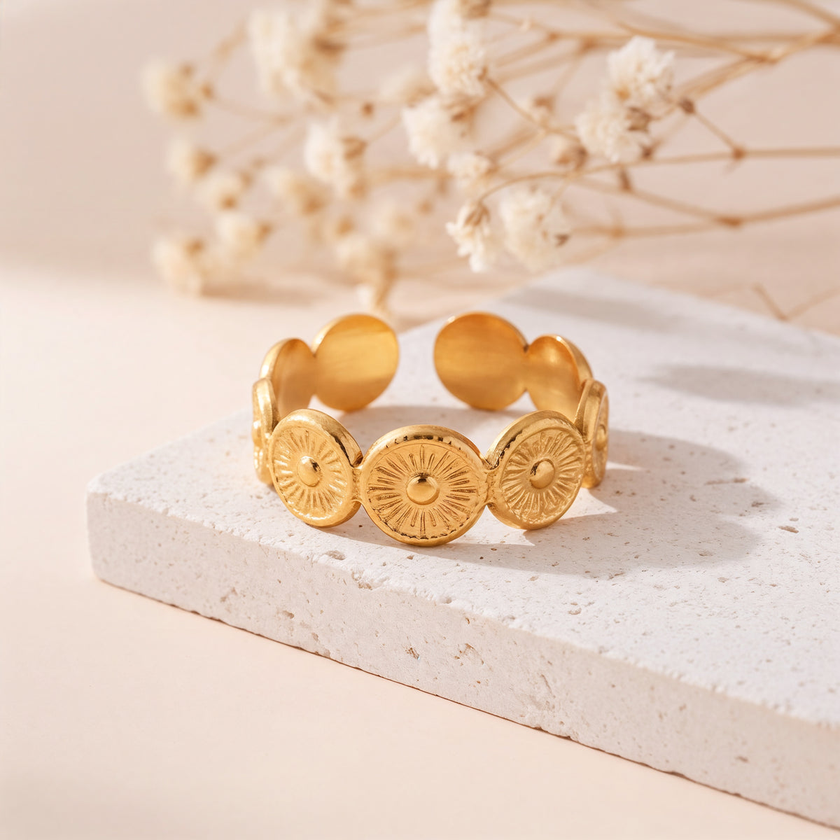 Statement-Ring aus Edelstahl 18 K vergoldet, offen und verstellbar, mit kreisförmigem Struktur-Design auf heller Steinplatte mit Trockenblumen – Aurema Ring | Mercy’s Jewelry