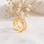 Strukturierter Doppelring aus Edelstahl 18 K vergoldet, offen und verstellbar, mit pyramidenförmigem Relief-Design auf hellem Stoff und Trockenblumen im Hintergrund – Sireva Ring | Mercy’s Jewelry