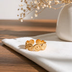 Symbol-Ring aus Edelstahl 14 K vergoldet mit Sonnendesign, verstellbar, liegt auf weißem Stoff auf Holztisch mit Trockenblumen im Hintergrund – Solare Ring | Mercy’s Jewelry