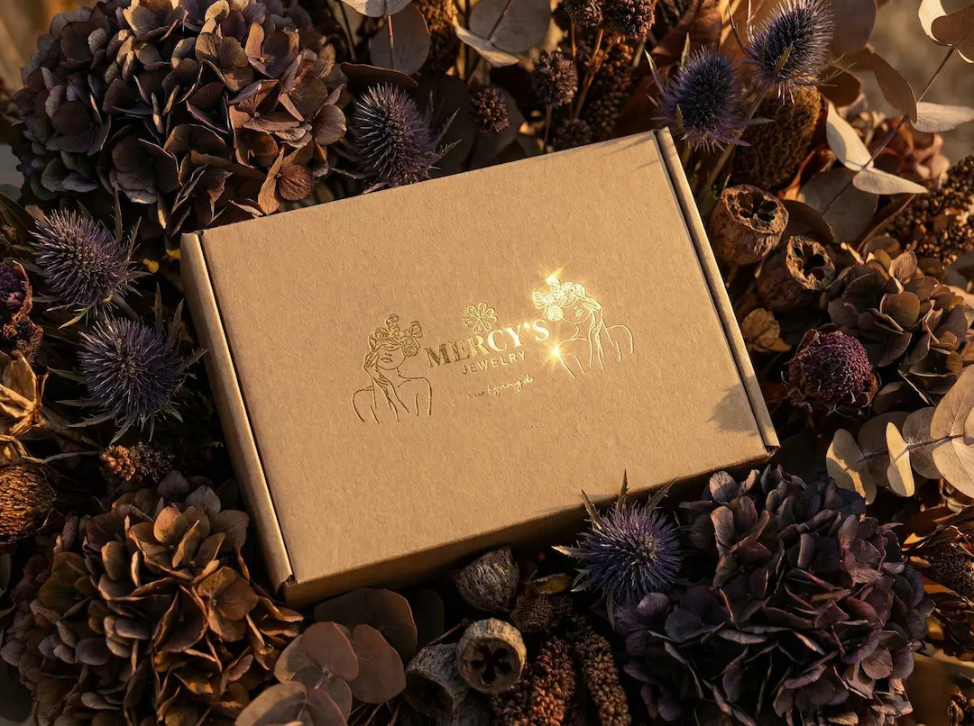MERCY’S Jewelry Unboxing-Box auf bymercy.de: Edle braune Box mit Goldprägung inmitten dunkler Trockenblumen.