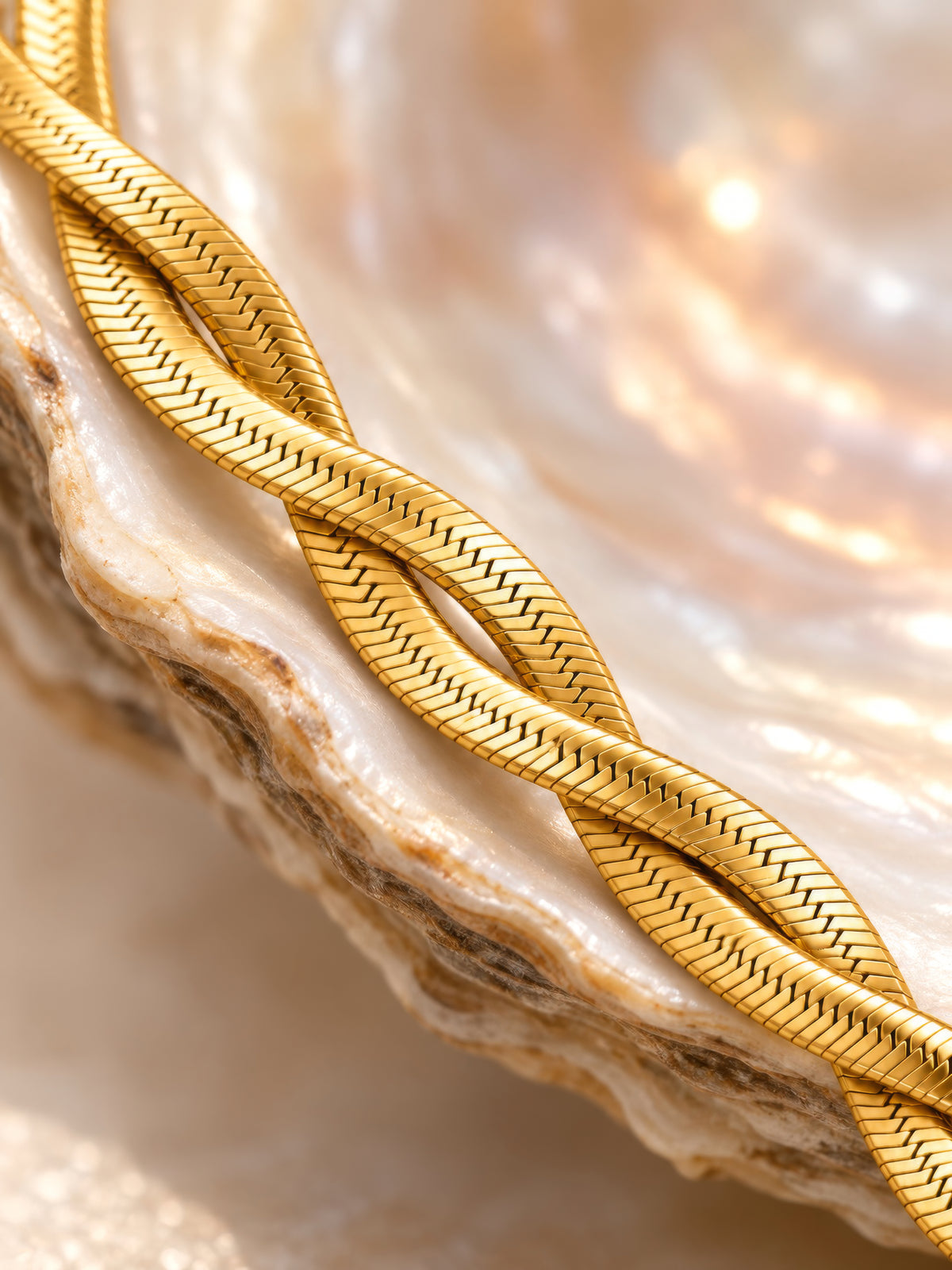 Makroaufnahme des Velira Double Armbands auf Perlmutt-Muschel, Detail der ineinander gedrehten goldenen Fischgrätenglieder