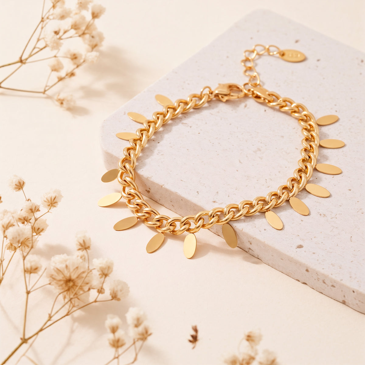 Vergoldetes Gliederarmband aus Edelstahl 18 K, mit ovalen Plättchen-Anhängerchen auf heller Steinplattform mit Trockenblumen – Marvella Armband | Mercy’s Jewelry