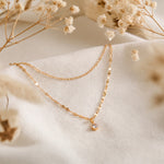 Zweireihige Halskette aus Edelstahl 18 K vergoldet mit feinem Zirkonia-Anhänger, liegt auf hellem Stoff mit Trockenblumen im Hintergrund – Lirae Layers Halskette | Mercy’s Jewelry