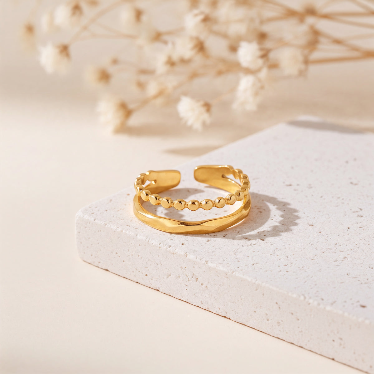 Zweireihiger Kugelring aus Edelstahl 18 K vergoldet, offen und verstellbar, mit glänzender Oberfläche auf heller Steinplattform mit Trockenblumen – Nayomi Ring | Mercy’s Jewelry