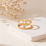 Zweireihiger Ring aus Edelstahl 18 K vergoldet, offen und verstellbar, mit gehämmerter Struktur auf heller Steinplattform und Trockenblumen im Hintergrund – Evaniah Ring | Mercy’s Jewelry