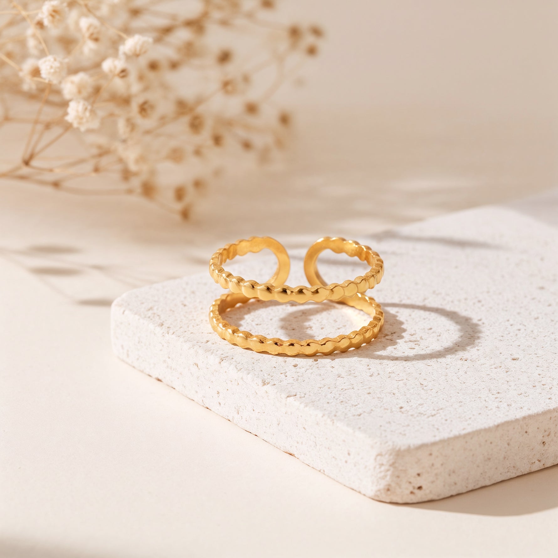 Zweireihiger Ring aus Edelstahl 18 K vergoldet, offen und verstellbar, mit gehämmerter Struktur auf heller Steinplattform und Trockenblumen im Hintergrund – Evaniah Ring | Mercy’s Jewelry